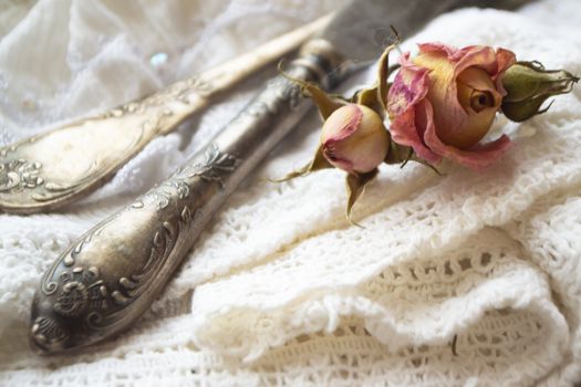 old silver fork with knife over the white vintage napkin and dry pink roses