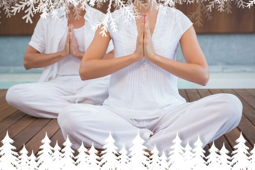 Couple in white sitting in lotus pose with hands together against fir tree forest and snowflakes