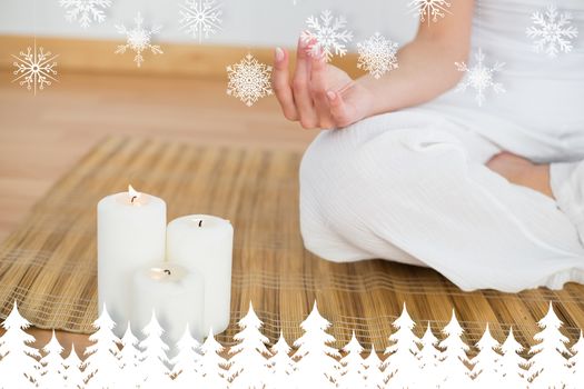 Woman sitting in lotus pose beside white candles against fir tree forest and snowflakes