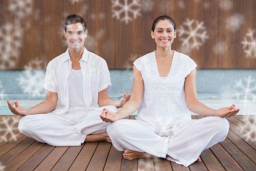 Attractive couple in white sitting in lotus pose smiling at camera against snowflakes