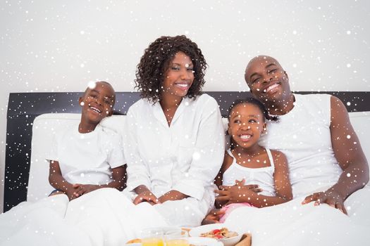 Happy family having breakfast in bed against snow falling