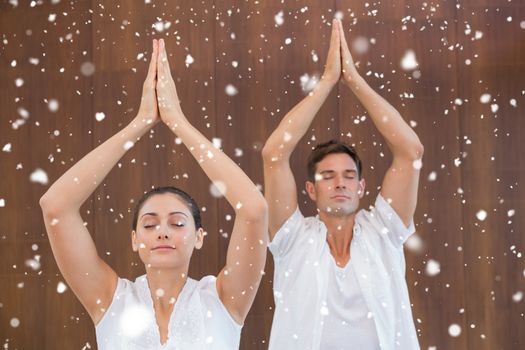Peaceful couple in white doing yoga together with hands raised against snow falling