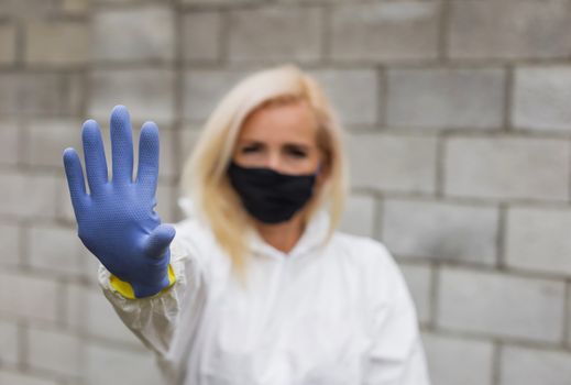 Woman in mask, white protective suit and gloves making sigh stop