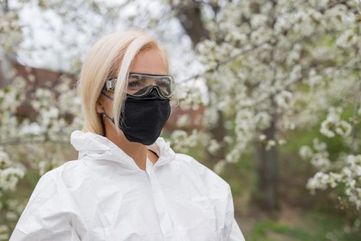 Woman in black mask and white protective suit at spring