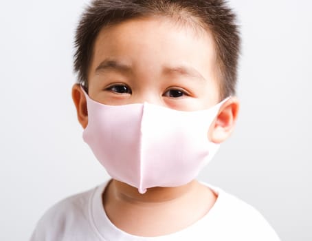 Portrait Asian little child boy wearing cloth face mask protective filter dust pm2.5, COVID-19 or coronavirus concept he looking to camera, studio shot isolated on white background with copy space