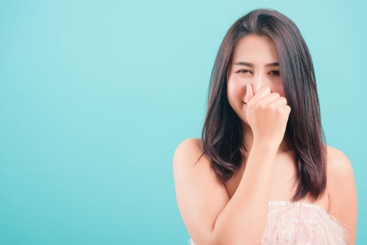 Asian happy portrait beautiful young woman standing smile her very bad smell use hand covers her nose on blue background with copy space for text