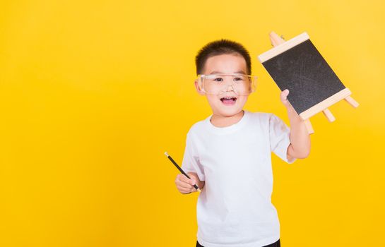 Asian Thai happy portrait cute little cheerful child boy smile he showing blackboard and looking to camera, studio shot isolated on yellow background with copy space