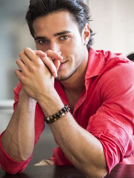 Attractive young man indoors wearing a shirt and beaded bracelets
