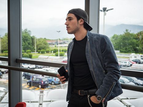 Attractive young man indoors wearing a denim jacket and baseball cap, reversed