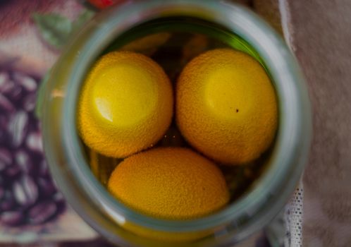 Three eggs in a jar full of yellow paint waiting to become colorful Еaster eggs.