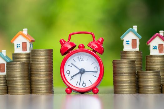 Red alarm clock And the house rests on coins. Placed on the table. Time investment concept Saving money to buy a house. Time of doing business Real estate. Schedule according to the planning schedule.
