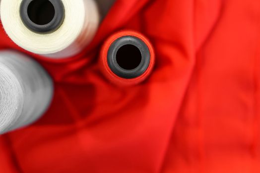 A multicolored thread spool placed on a red fine fabric. Fashion designer room, background and texture.