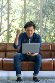 Asian man spend holidays in the living room. The young man wore comfortable clothes use laptop computer to search for jobs, and he got a job.