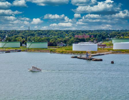 A luxury pleasure boat past fuel tanks on the shore