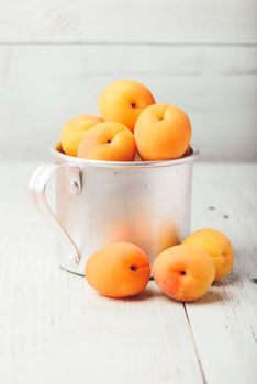 Mellow apricots in metal mug over light wooden surface