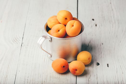 Mellow apricots in metal mug over light wooden surface