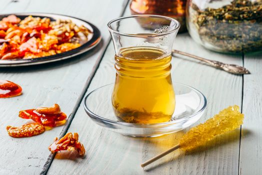 Green tea in armudu glass with oriental nut delights on metal plate over light wooden surface