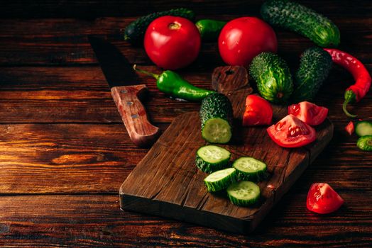 Sliced vegetables. Tomatoes, cucumbers and chili peppers over wooden background.