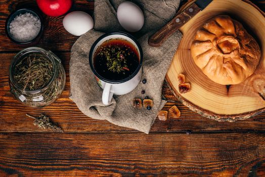 Rustic breakfast with traditional tatar pastry elesh, herbal tea in metal mug, apple and boiled eggs over dark wooden surface