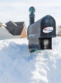 Metal mailbox for rural homes buried in deep snow with I Voted sticker as concept for voting by mail or absentee ballot paper