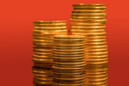 Focus on a stack of gold coins with other coin stacked in the background out of focus against red backdrop