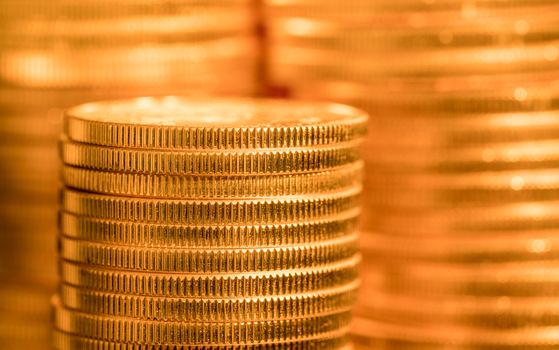 Focus on a stack of gold coins with other coin stacked in the background out of focus