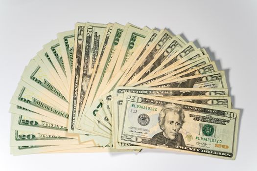 Thousands of US dollars laid out in a fan shape with 20 dollar bills against a white background