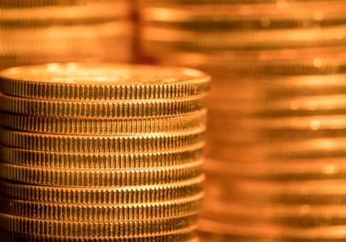 Focus on a stack of gold coins with other coin stacked in the background out of focus
