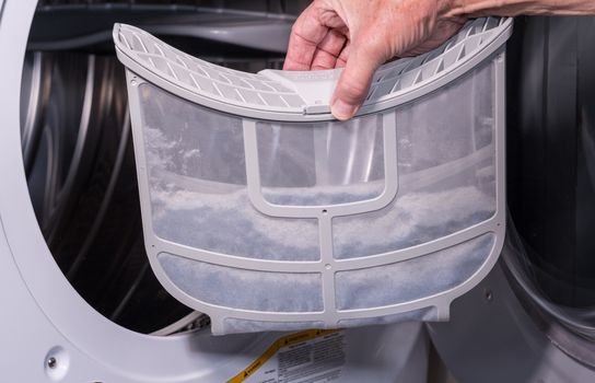 Senior caucasian man holding the lint filled trap from a front loading tumble dryer