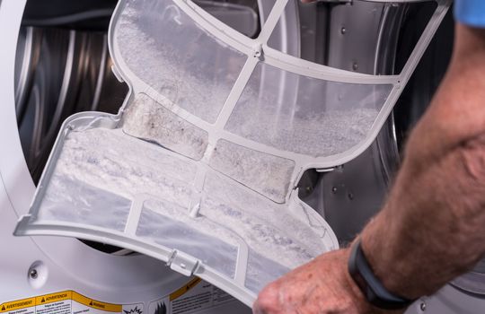 Senior caucasian man holding the lint filled trap from a front loading tumble dryer