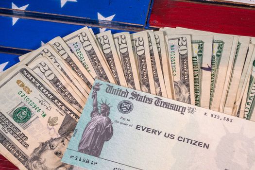 Stack of 20 dollar bills with illustrative coronavirus stimulus payment check on USA flag