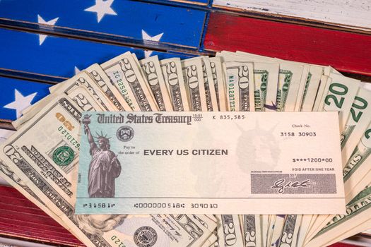 Stack of 20 dollar bills with illustrative coronavirus stimulus payment check on USA flag