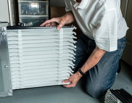 Senior caucasian man checking a clean folded air filter in the HVAC furnace system in basement of home