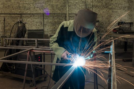 Welder welding a metal part in an industrial environment, wearing standard protection equipment. Sparks flying, fumes, industrial background