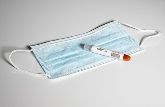 Positive blood test for Coronavirus laying on doctor surgical mask to show danger to front line medical workers