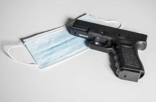 Pistol gun laying on top of medical mask in concept for dangers faced by front line medical personnel