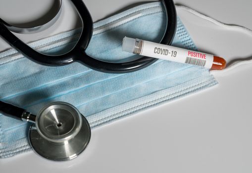 Positive blood test for Coronavirus laying on doctor surgical mask with stethoscope to show danger to front line medical workers