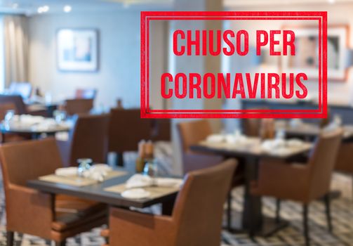 Defocused view of interior of an upmarket restaurant empty and closed with Italian notice saying Closed due to Coronavirus