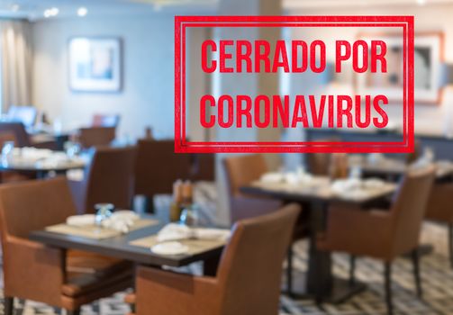 Defocused view of interior of an upmarket restaurant empty and closed with spanish notice saying Closed due to Coronavirus