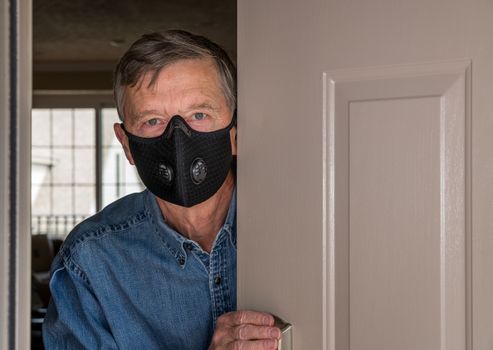 Senior man with face mask looking worried at front door in case visitors bring coronavirus to his home
