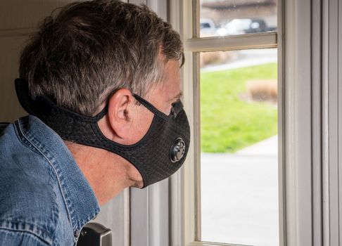 Senior man with face mask looking worried at front door in case visitors bring coronavirus to his home
