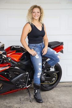 Young blond woman, leaning on her sport motocycle, in font of a garage door