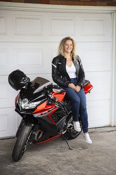 young woman leaning on a sport motocycle in front of a garage door