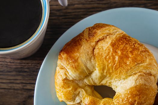 single croissant on a plate with a cup of coffee