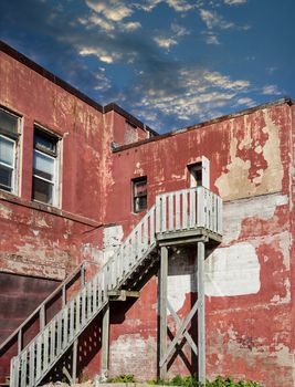 Rickety wooden stairs on side of an old peeling red plaster building under clear blue sky