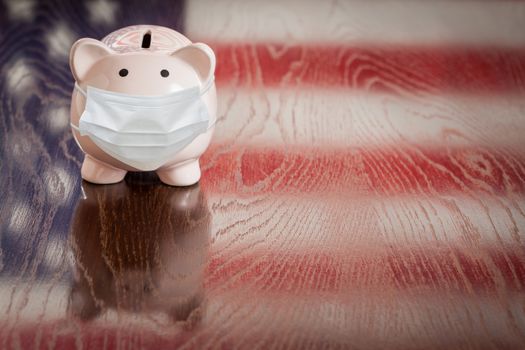 Piggy Bank Wearing Medical Face Mask With American Flag Reflecting on Table.