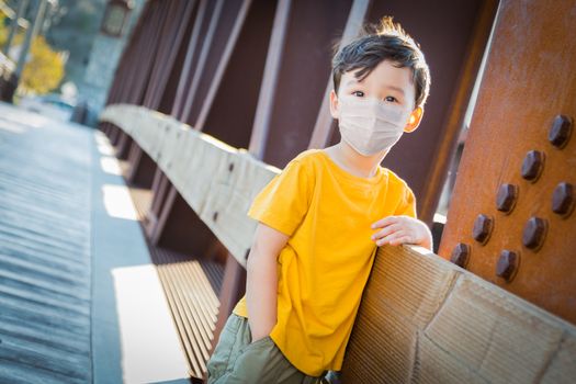 Young Mixed Race Chinese and Caucasian Boy Playing Alone Wearing Medical Face Mask Outside.