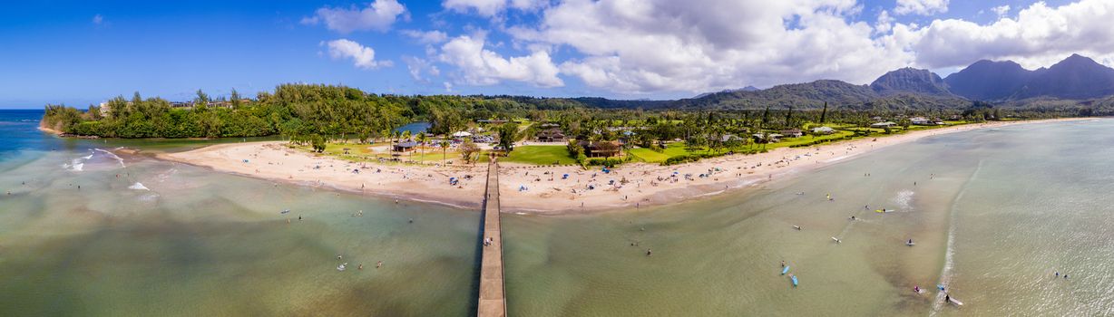 Aerial panoramic image off the coast over Hanalei Bay and pier on Hawaiian island of Kauai with surfers in the water