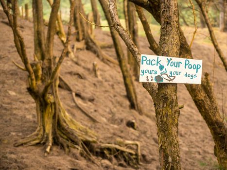 Pick up or pack your poop sign on tree advising people to not leave waste on the ground in forest
