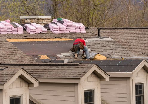 Roofing contractor removing the old tiles before replacing with new shingles on a townhouse roof